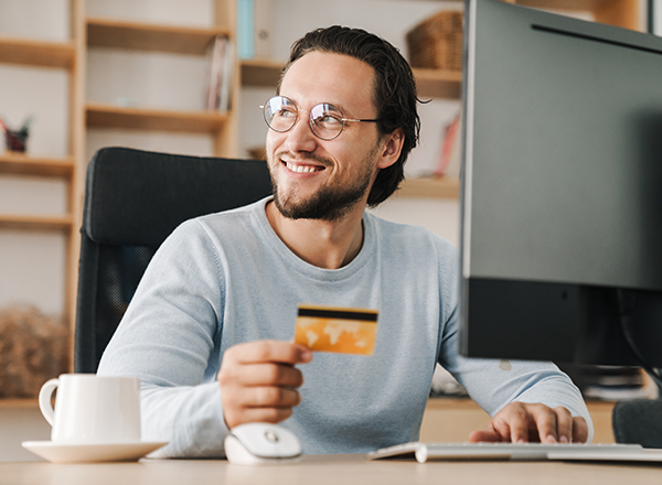 indiviudal male sitting at computer with coffee and credit card with a smile on his face looking out the window